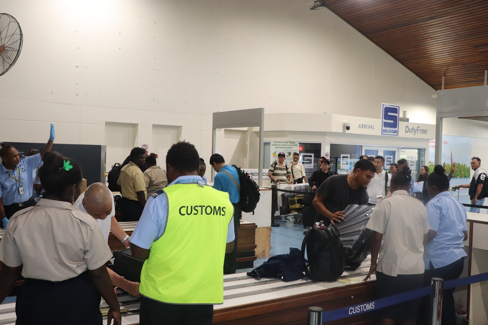 Customs officers inspecting arriving passenger baggage at Honiara International Airport