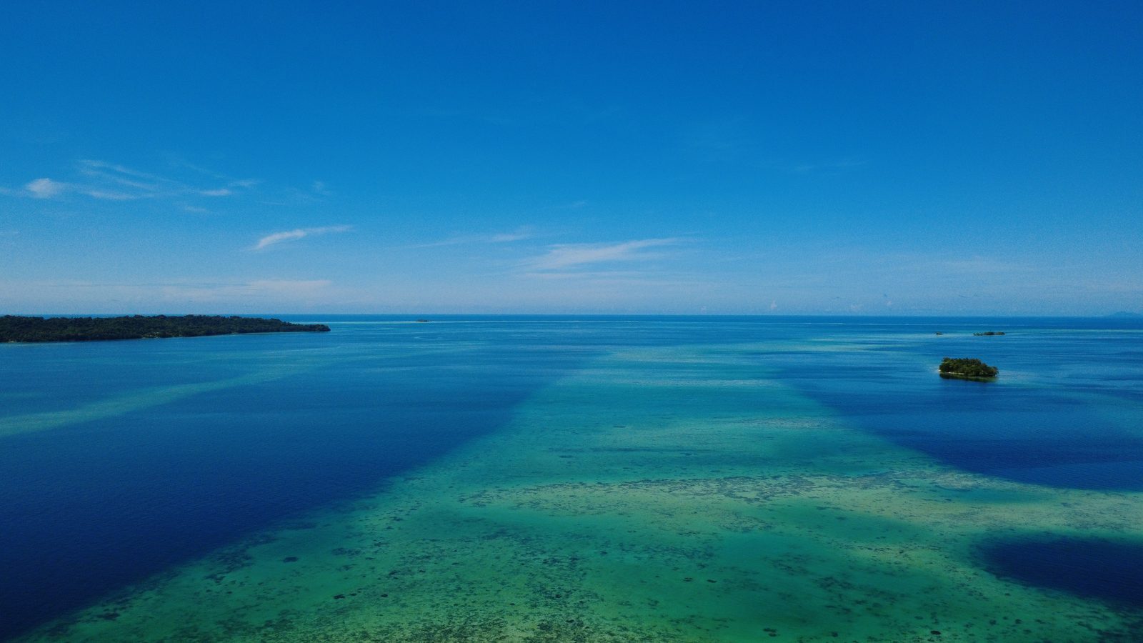 Small forested island surrounded by turquoise reef water